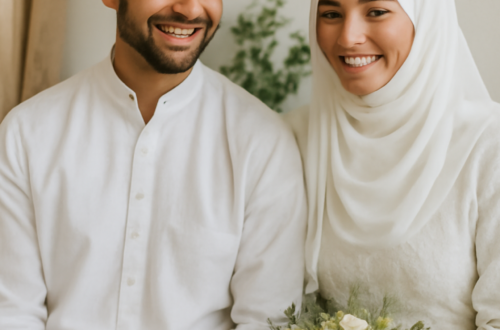 A joyful newlywed Muslim couple smiling happily together in simple wedding attire, seated side by side. The bride wears a white lace dress and hijab, holding a bouquet of cream-colored roses. The groom wears a white kurta and taqiyah cap.